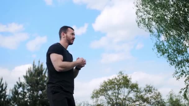 Silny mężczyzna z muskulaturą rozgrzewa ręce przed treningiem na tle zielonych drzew z pięknym niebem. - Materiał filmowy, wideo