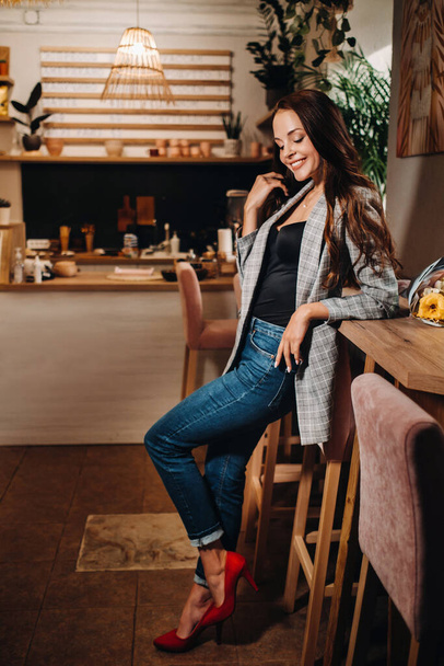 Portrait of a young European girl with long hair in a coffee shop in the evening light, a tall Girl in a jacket with long hair in a cafe. - Foto, afbeelding