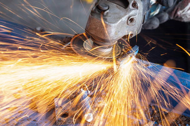 worker cutting steel with grinding machine and splashes of sparks in workshop. - Photo, Image