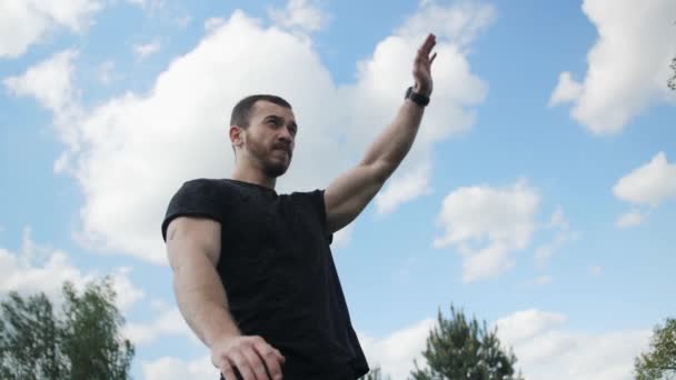 Sportsman does warm-up stretching hands arms before training on a background of green trees with a beautiful sky. - Footage, Video