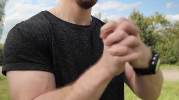 Strong man with muscular does warm-up stretching hands arms before training on a background of green trees with a beautiful sky. - Footage, Video