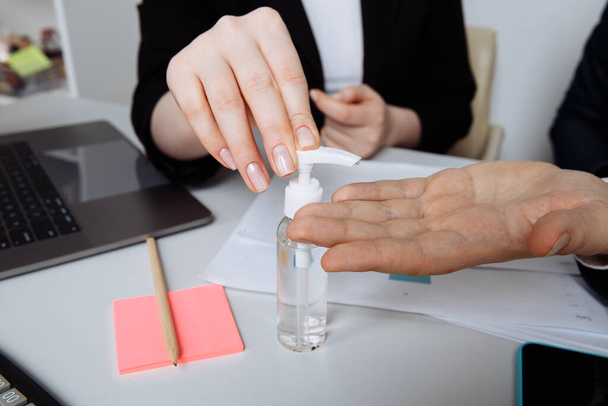 Detailní záběr rukou pomocí antiseptického gelu dezinfikovat ruce přes pracovní stůl v kanceláři. Preventivní opatření v období epidemie a sociálního vyloučení. - Fotografie, Obrázek