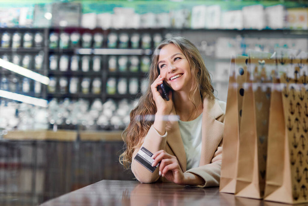 Online shopping concept. Woman with shopping paper bags in cafe talking on phone. - 写真・画像