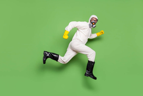 Full body profile side photo of doctor man jump run dream disinfect home stop ncov epidemic wear white suit hazmat yellow latex gloves goggles isolated green color background - Foto, immagini