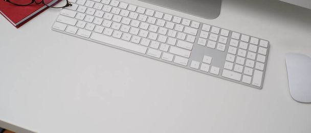 Bilgisayarlı, gözlüklü, not defterli ve beyaz masadaki basit ofis masasının kırpılmış görüntüsü - Fotoğraf, Görsel
