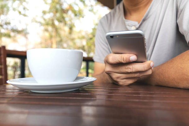 closeup of smartphones in the hands of a man sitting in a coffee shop with soft-focus and over light in the background - Photo, image