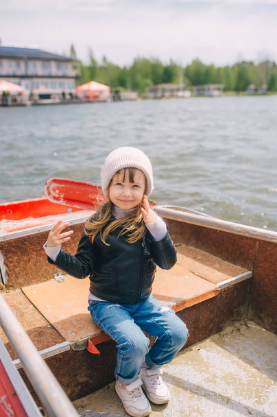 Pieni tyttö, jolla oli vaaleat hiukset ja eurooppalainen ulkonäkö ja joka poseerasi veneessä joella. Kelluen aurinkoisena kevätpäivänä. - Valokuva, kuva