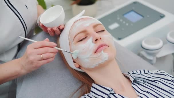 Średnie ujęcie kosmetyczki zakładającej kremową maskę na twarz kobiet w salonie piękności - Materiał filmowy, wideo