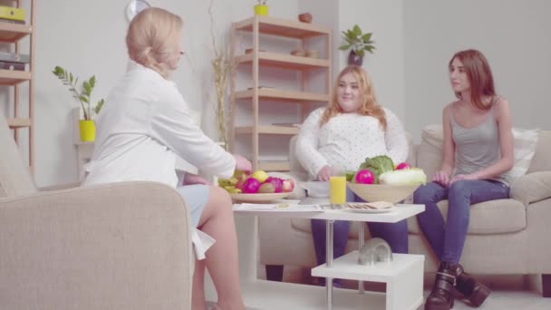 The nutritionist after listening to the patients gives them fruits explaining their positive properties. Proper nutrition concept. Toned footage. Prores 422 - Materiał filmowy, wideo