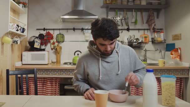 A young man having breakfast in the kitchen. Man eats Corn Flakes Cereal - Video, Çekim