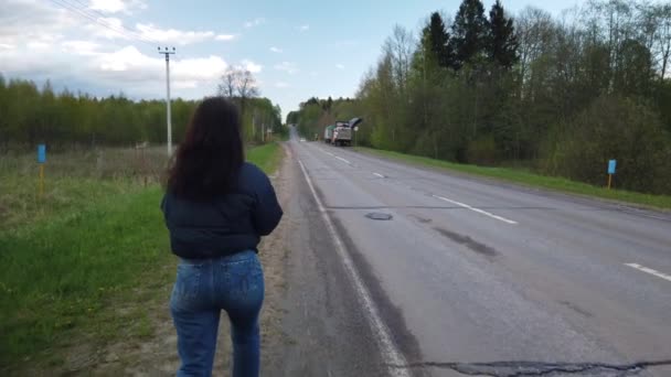 Dívka kráčí po prázdné silnici a snaží se chytit auto stopování - Záběry, video