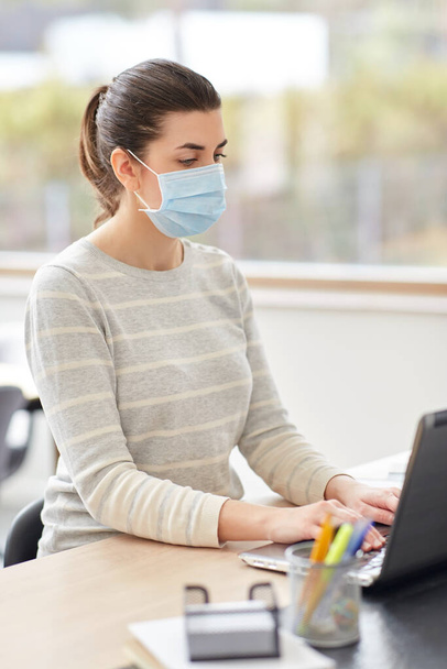 woman in mask with laptop working at home office - Foto, Bild