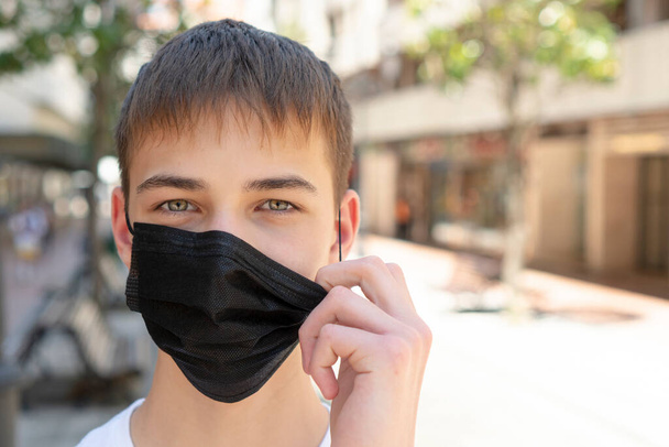 Triste jeune homme enlève un masque noir médical près de la route dans une rue vide de la ville sans personne. Seule. Copyspace. Gros plan. Concept de protection contre le coronavirus
 - Photo, image