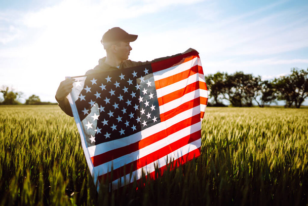 Fourth of July. Patriotic man with the national American flag in the field. Young man proudly waving an American flag. Independence Day.  - Photo, image