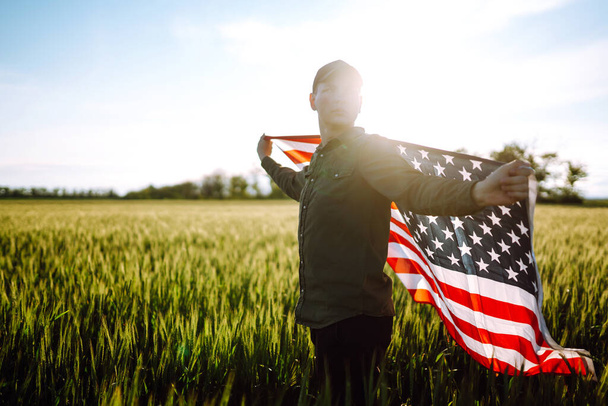 Fourth of July. Patriotic man with the national American flag in the field. Young man proudly waving an American flag. Independence Day.  - Fotó, kép