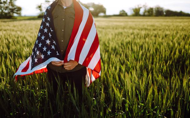 Vierter Juli. Patriotischer Mann mit der amerikanischen Nationalflagge auf dem Feld. Ein junger Mann schwenkt stolz eine amerikanische Flagge. Unabhängigkeitstag.  - Foto, Bild