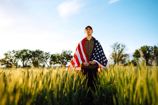 Fourth of July. Patriotic man with the national American flag in the field. Young man proudly waving an American flag. Independence Day.  - Zdjęcie, obraz
