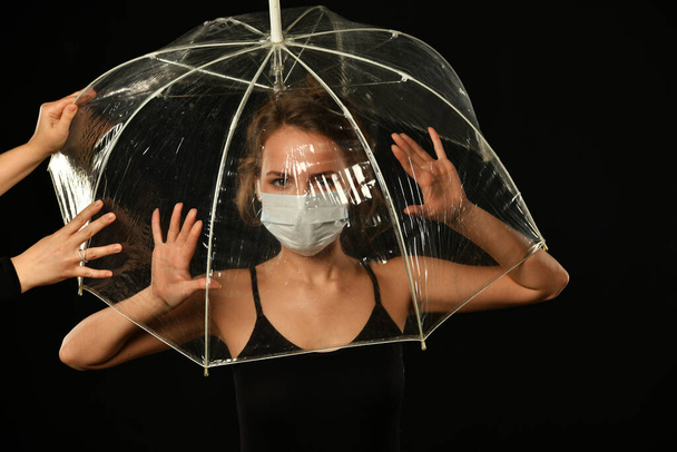 meisje in het zwart in een beschermende medische masker is op zoek naar een uitweg uit een transparante cap - Foto, afbeelding