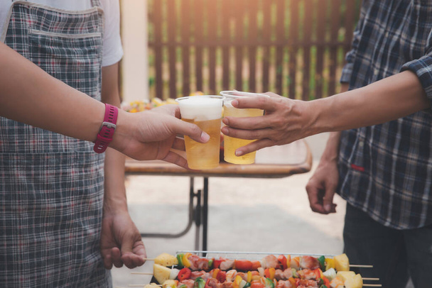 Junge Männer bejubeln einen Drink bei einer Grillparty unter Freunden. Essen, Trinken, Menschen und Familienzeitkonzept. - Foto, Bild