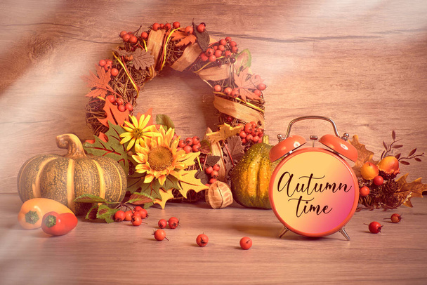 目覚まし時計テキスト秋時間。環境に優しいゼロ無駄素朴な装飾。秋の葉、黄色の花、装飾的な花輪、秋の葉とベリー。自然の秋感謝祭の収穫の装飾. - 写真・画像