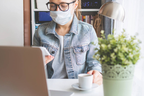 girl sits at a desk in a medical mask and holds a phone in her hand - Foto, Imagen