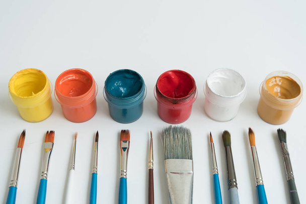 Open jars with gouache and paint brushes of different sizes. The view from the top. Background, texture. The concept of space for creativity - 写真・画像