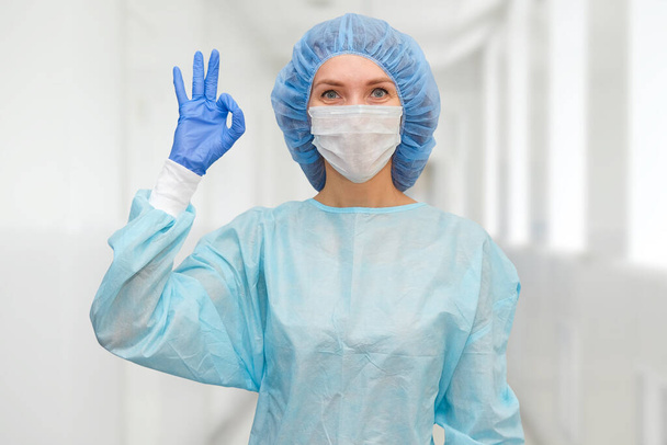 Portrait of doctor in scrubs. A female doctor in a protective cap and face mask in safety measures against the coronavirus. - Photo, Image