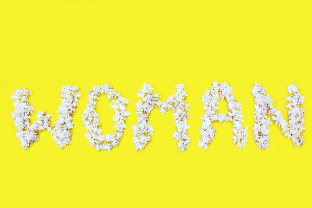 La inscripción Mujer está escrita en flores blancas de color lila sobre un fondo amarillo. La palabra Mujer está escrita con flores lila. Inscripción floral Mujer. Fondo para una tarjeta de felicitación
. - Foto, imagen