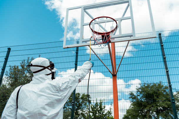 cleaning specialist in hazmat suit and respirator disinfecting basketball court during coronavirus pandemic - Photo, Image