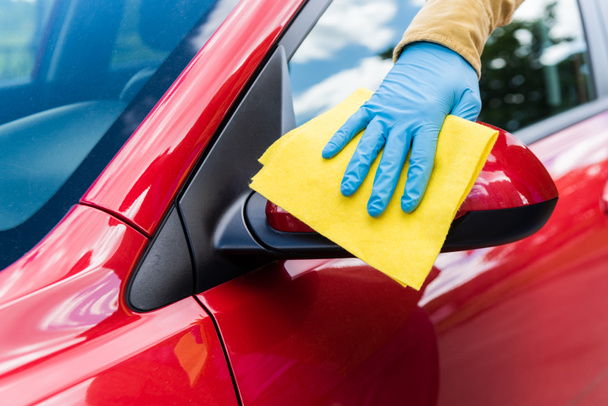 bijgesneden beeld van de mens in latex handschoen met behulp van doek voor het reinigen van de auto tijdens het coronavirus pandemie - Foto, afbeelding