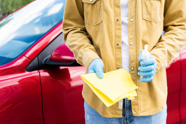 vue recadrée du jeune homme dans des gants en latex en utilisant antiseptique et chiffon pour nettoyer la voiture pendant la pandémie de coronavirus
 - Photo, image