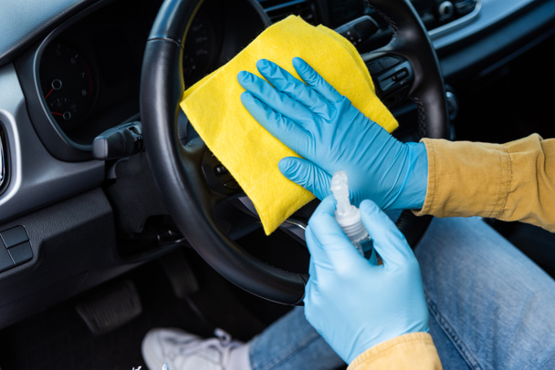 visão cortada do homem em luvas de látex usando anti-séptico e pano para limpar o interior do carro durante a pandemia de coronavírus
 - Foto, Imagem