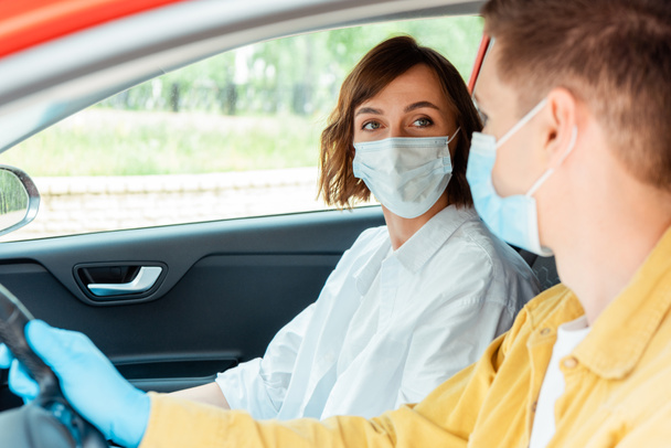 hombre y mujer con máscaras médicas y guantes de protección sentados en el coche durante la pandemia de covid-19
 - Foto, Imagen