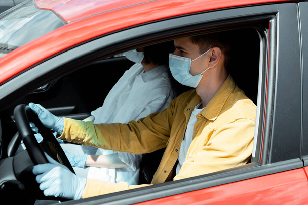 hombre y mujer con máscaras médicas y guantes de protección sentados en el coche durante la pandemia de coronavirus
 - Foto, Imagen