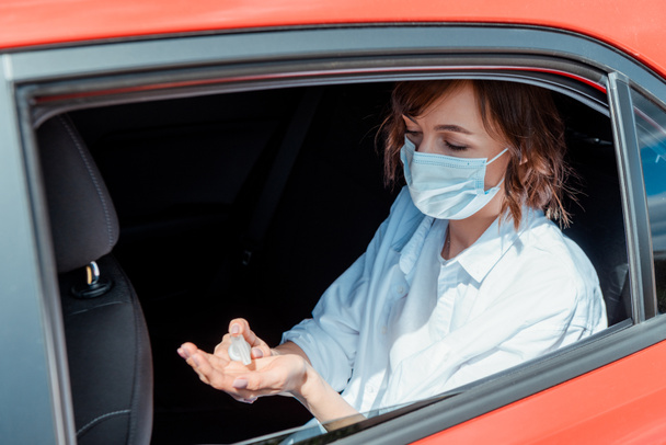 κορίτσι σε ιατρική μάσκα χρησιμοποιώντας αντισηπτικό στο αυτοκίνητο κατά τη διάρκεια της πανδημίας coronavirus - Φωτογραφία, εικόνα