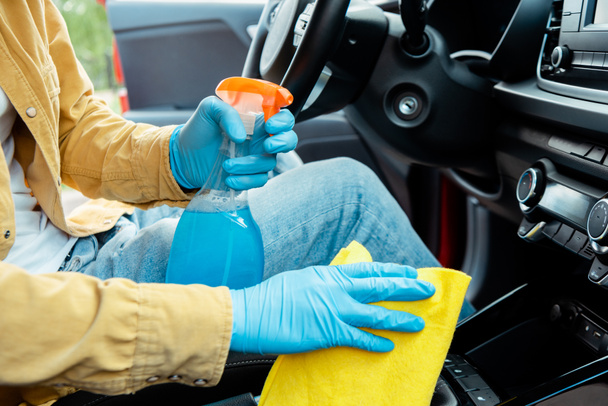 visão parcial do homem em luvas de látex usando spray anti-séptico e pano para limpar o interior do carro durante a pandemia de covid-19
 - Foto, Imagem
