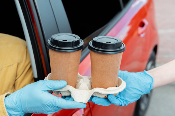 vista recortada del hombre en guantes de protección comprar café para ir desde el coche durante la pandemia covid-19
  - Foto, Imagen