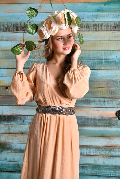 spring girl in a beige dress and a floral wreath on her head posing in the window opening - Photo, Image