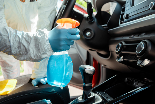 cropped view of specialist in hazmat suit cleaning car interior with antiseptic spray during coronavirus pandemic - Photo, Image