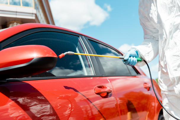 visão cortada de especialista em carro de limpeza de terno hazmat com spray desinfetante durante a pandemia de coronavírus
 - Foto, Imagem