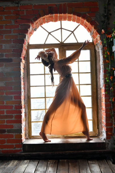 spring girl in a beige dress and a floral wreath on her head posing in the window opening - Foto, Imagen