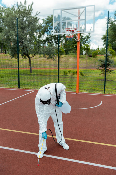 spécialiste en combinaison de danger et respirateur désinfectant terrain de basket dans le parc pendant la pandémie covid-19
 - Photo, image