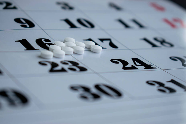 薬で概念的な写真。カレンダーの背景に白い丸薬. - 写真・画像
