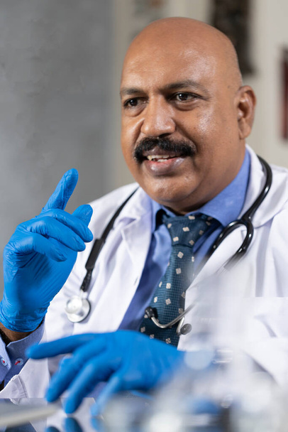 Um médico explica a um paciente em sua clínica usando um par de luvas azuis
 - Foto, Imagem