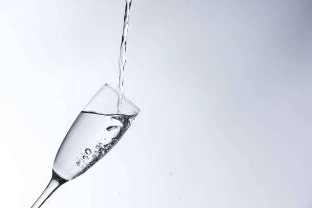 Čirá pitná voda padá do čiré sklenice, zdravé, zdravé, sladké vody bez zápachu nebo chuti. Po hladině stékaly kapky vody. Proud vody vstupující do skla - Fotografie, Obrázek