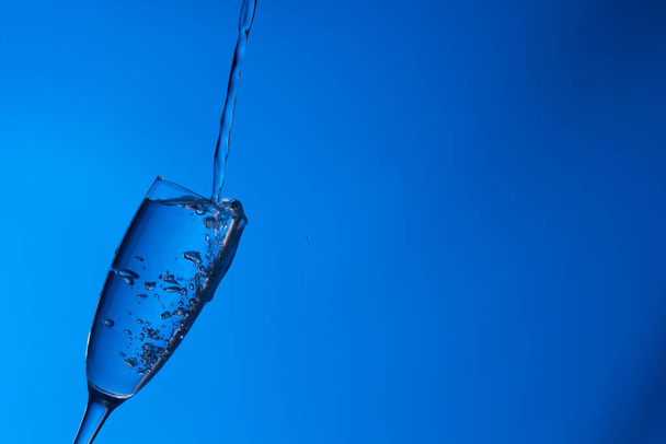 Tiszta, ivóvíz esik egy tiszta pohár, egészséges, egészséges, friss víz szaga és íze nélkül. Vízcseppek fröccsennek a felszínre. Az üvegbe belépő víz sugara - Fotó, kép