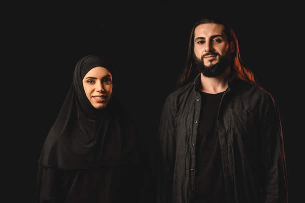 Χαμογελαστό μουσουλμανικό ζευγάρι κοιτάζοντας κάμερα απομονωμένη σε μαύρο  - Φωτογραφία, εικόνα