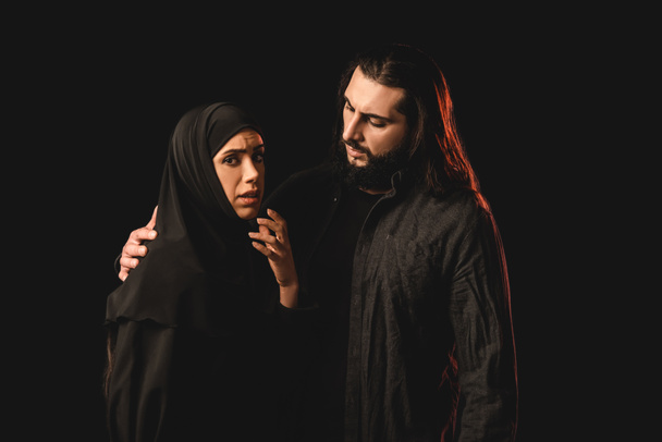 Moslim man omarmen bezorgd vrouw geïsoleerd op zwart  - Foto, afbeelding