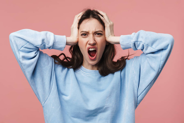 Image of displeased brunette woman wearing casual shirt frowning and grabbing her head isolated over pink background - Foto, imagen