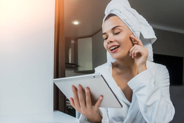 Young beautiful woman in white towel and robe holding a tablet. Morning of a woman at home concept. - Fotó, kép